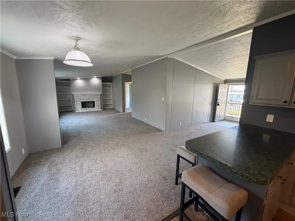 Dining space featuring crown molding, dark colored carpet, a textured ceiling, a stone fireplace, and built in features