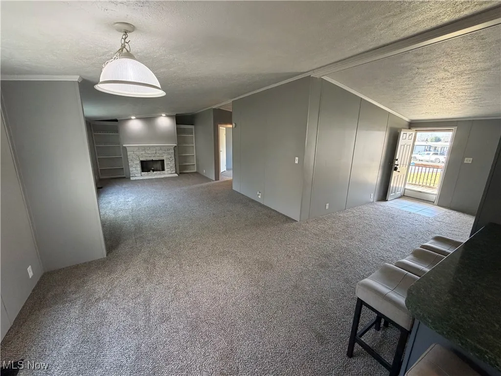 Unfurnished living room with crown molding, carpet floors, a textured ceiling, built in features, and a stone fireplace