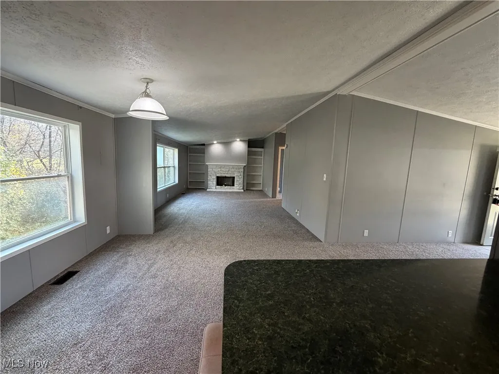 Unfurnished living room with ornamental molding, a stone fireplace, a textured ceiling, light carpet, and a decorative wall