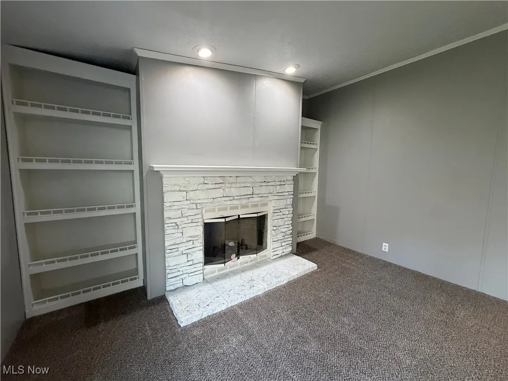 Unfurnished living room featuring dark carpet, ornamental molding, a fireplace, and a decorative wall