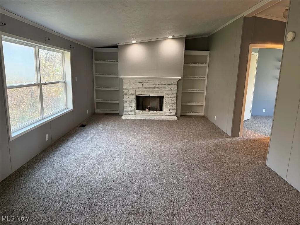 Unfurnished living room featuring crown molding, carpet floors, a stone fireplace, a textured ceiling, and lofted ceiling