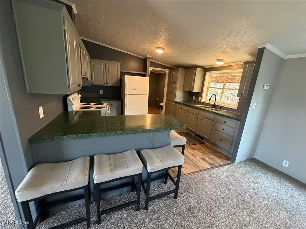 Kitchen featuring vaulted ceiling, a breakfast bar, a textured ceiling, a peninsula, and white appliances