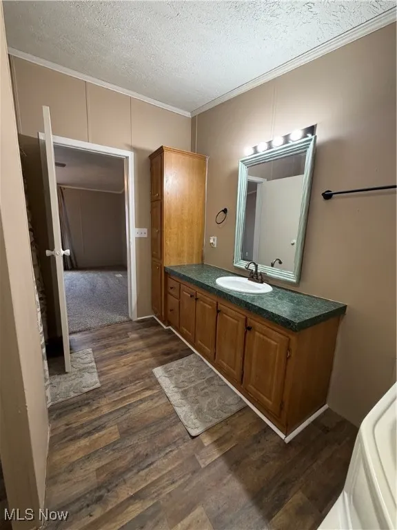 Full bathroom featuring ornamental molding, vanity, a textured ceiling, and dark wood-style flooring