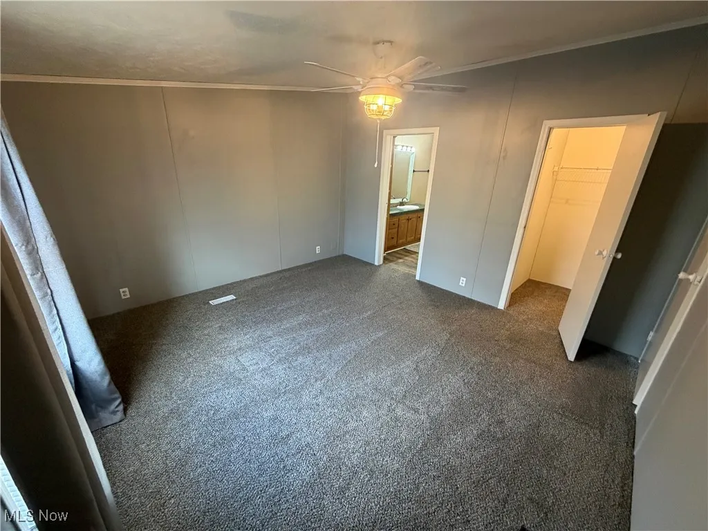 Unfurnished bedroom featuring ornamental molding, dark colored carpet, a spacious closet, ceiling fan, and connected bathroom
