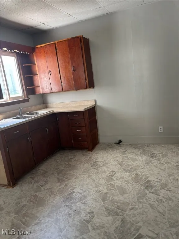 Kitchen featuring light stone finish floors, light countertops, open shelves, dark brown cabinets, and a paneled ceiling