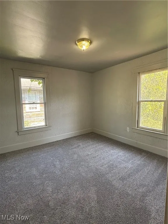 Spare room with a textured wall and dark colored carpet