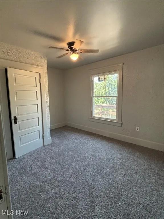 Unfurnished room featuring dark carpet, a textured ceiling, a ceiling fan, and a textured wall
