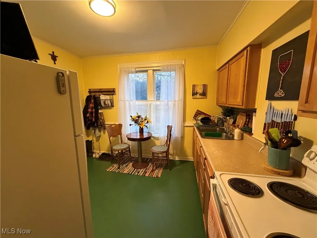 Kitchen featuring white appliances, brown cabinets, ornamental molding, and light countertops