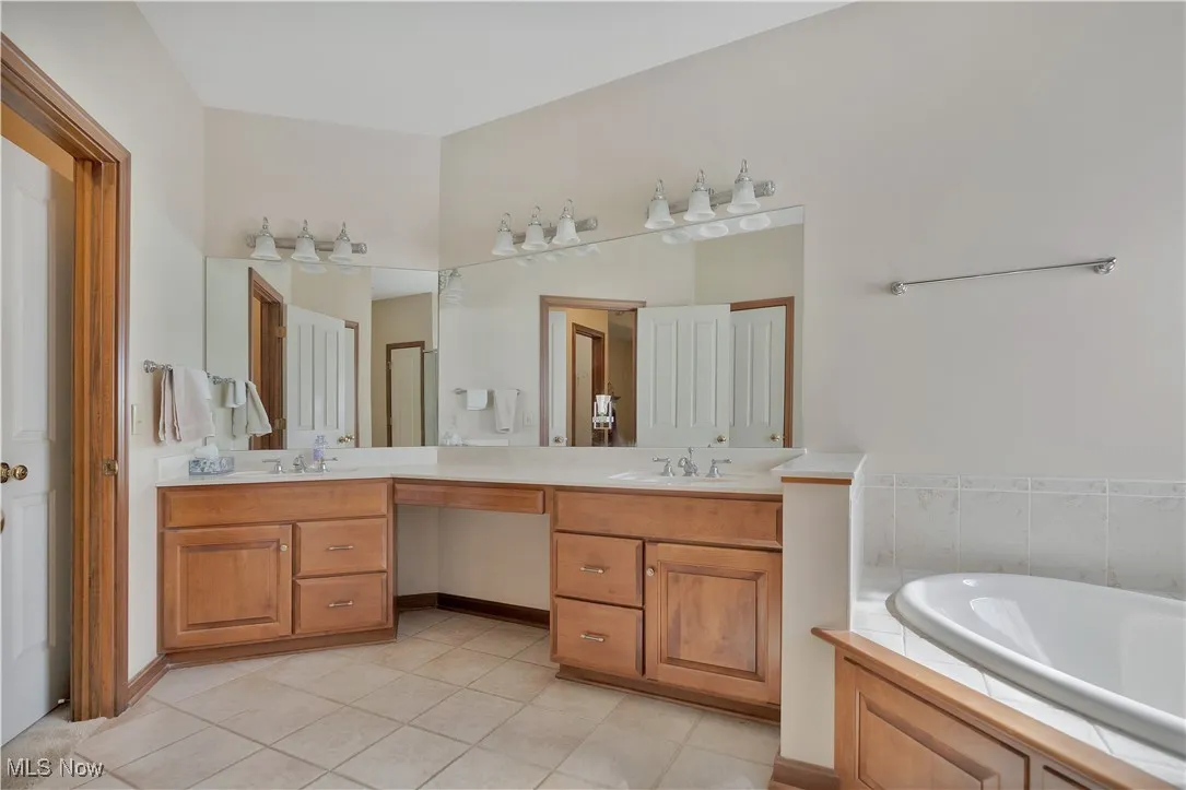 Full bath with double vanity, light tile patterned floors, and a bath