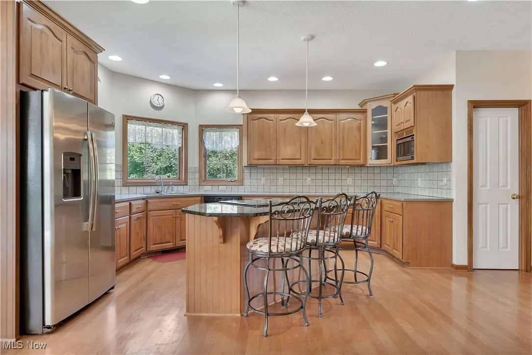Kitchen with stainless steel appliances, a breakfast bar area, glass insert cabinets, pendant lighting, and light wood finished floors
