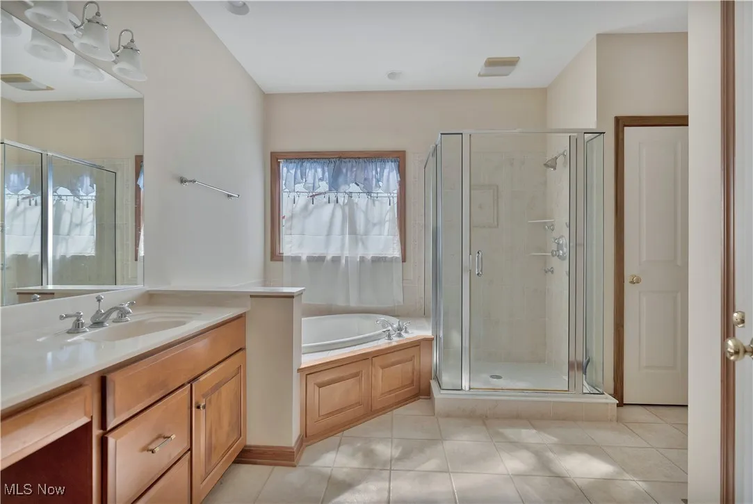 Full bathroom featuring a shower stall, a garden tub, vanity, and light tile patterned flooring with separate water closet