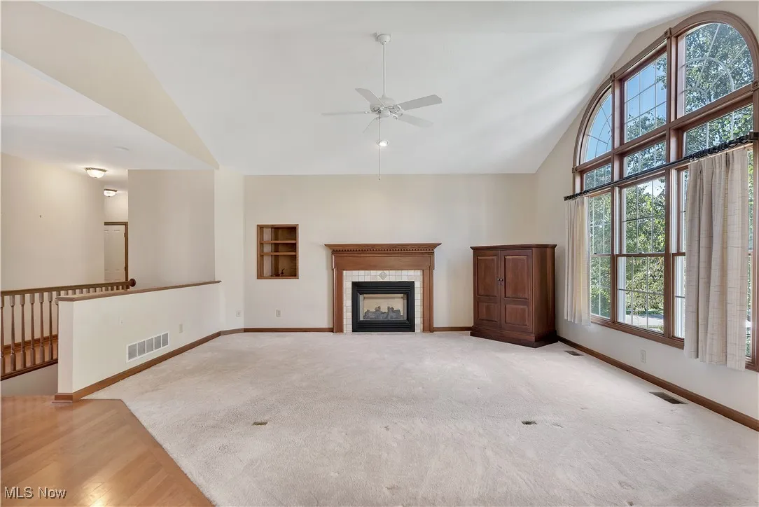 Living room with a tile fireplace, high vaulted ceiling, a ceiling fan, and natural light.