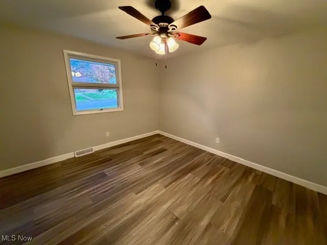 Empty room with dark wood-style flooring and a ceiling fan