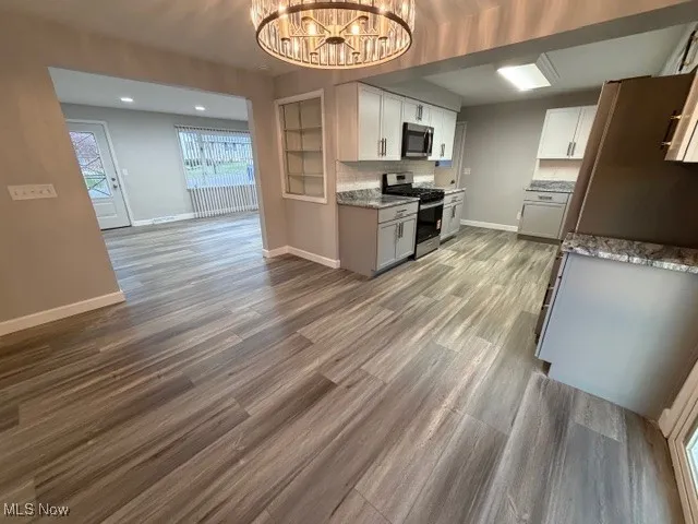 Kitchen with stove, light stone counters, light wood-style flooring, a chandelier, and tasteful​​‌​​​​‌​​‌‌​‌‌​​​‌‌​‌​‌​‌​​​‌​​ backsplash