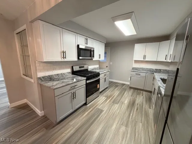 Kitchen with stainless steel appliances, backsplash, light wood-style floors, and white cabinetry