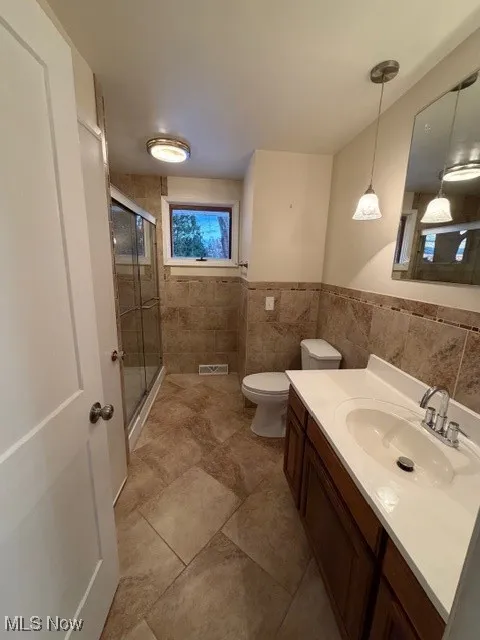 Full bath with a stall shower, vanity, tile walls, and a wainscoted wall