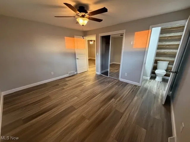 Unfurnished bedroom featuring dark wood-type flooring, a closet, a ceiling fan, and connected bathroom