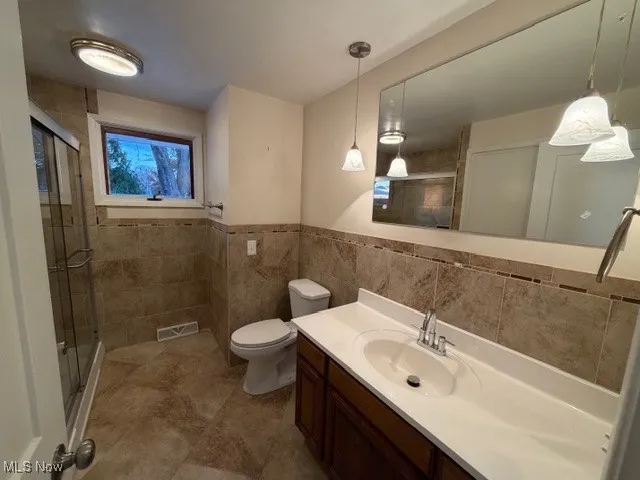 Full bathroom with tile walls, vanity, a shower stall, and a wainscoted wall