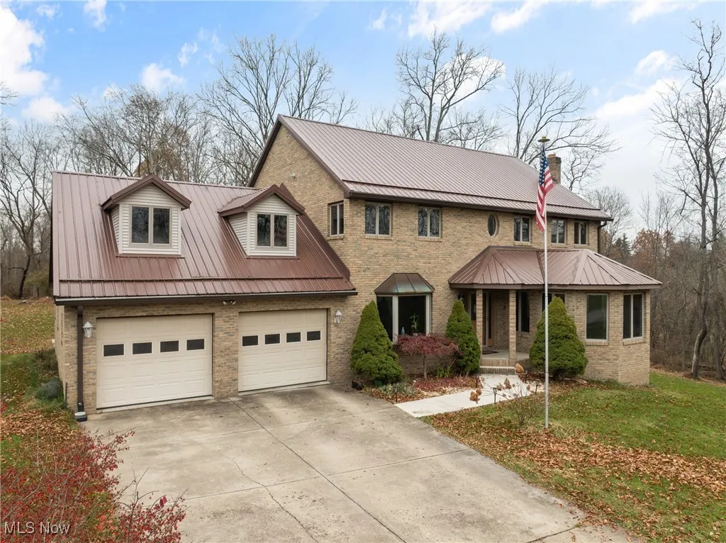 View of front facade featuring brick siding, driveway, a chimney, and a metal roof