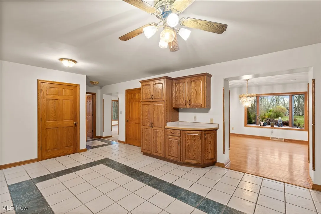 Kitchen with brown cabinets, light tile patterned flooring, light countertops, inlaid floor details, and ceiling fan