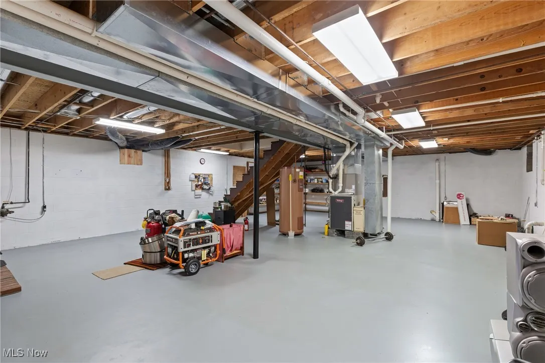 Unfinished below grade area featuring heating unit, water heater, and stairs