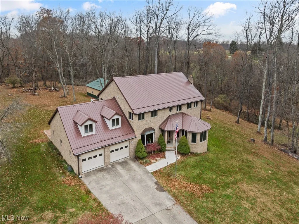 View of front facade with a front yard, driveway, a garage, a wooded view, and a metal roof