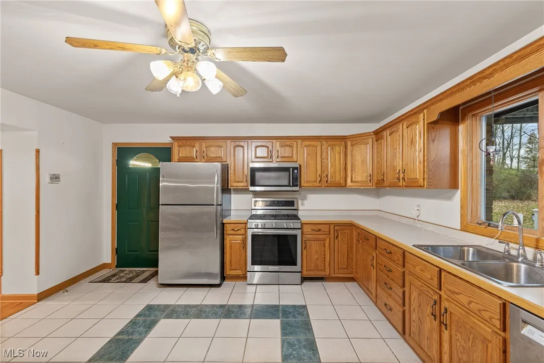 Kitchen with light tile patterned floors, appliances with stainless steel finishes, light countertops, ceiling fan, and brown cabinets