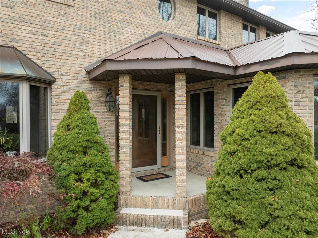 View of exterior entry featuring covered porch, brick siding, and a metal roof