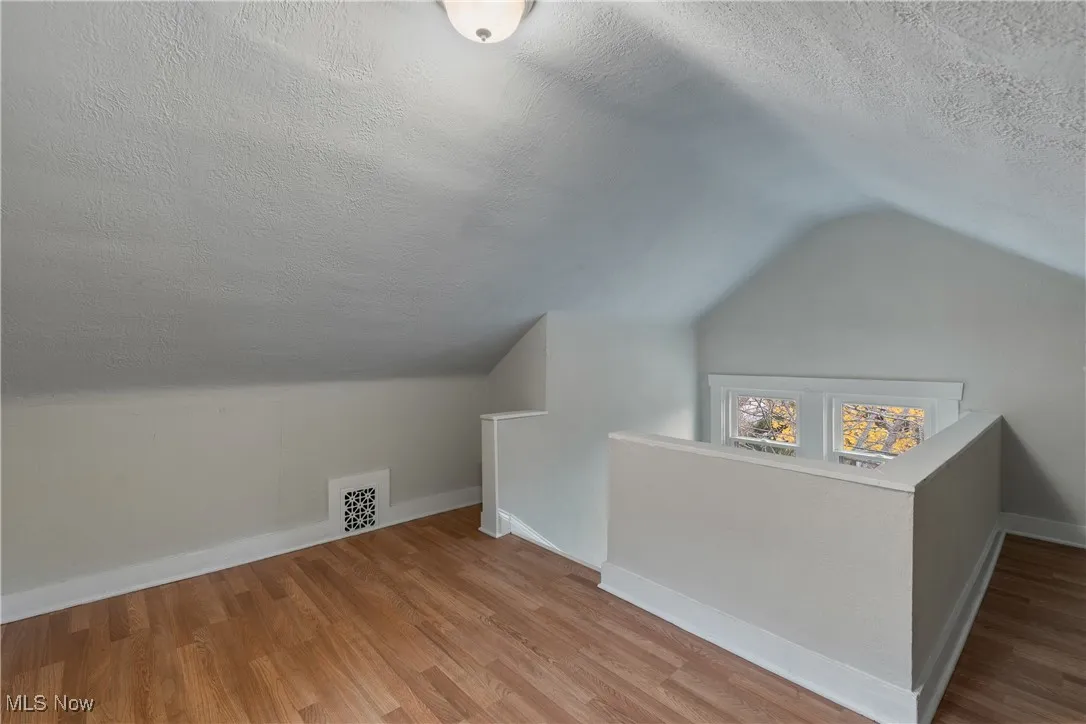 Bonus room with a textured ceiling, vaulted ceiling, and wood finished floors