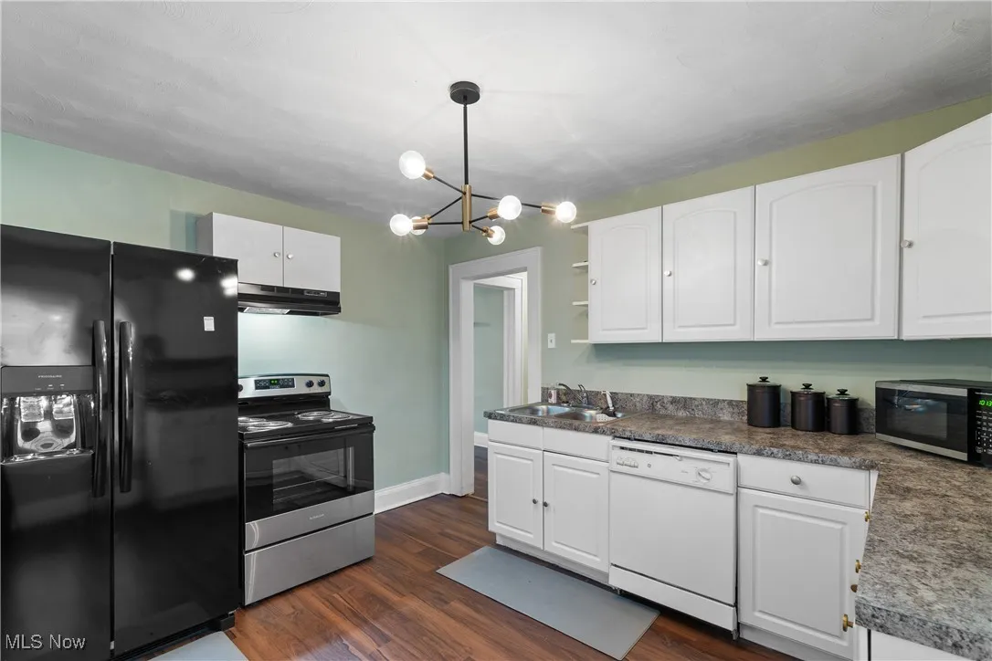 Kitchen featuring stainless steel appliances, white cabinets, dark wood-style flooring, hanging light fixtures, and a chandelier