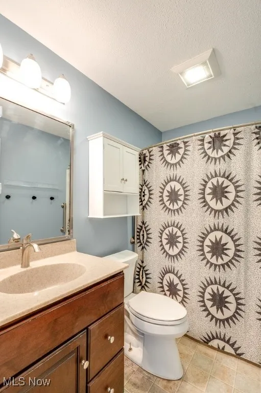 Full bathroom with vanity, a textured ceiling, curtained shower, and light tile patterned floors