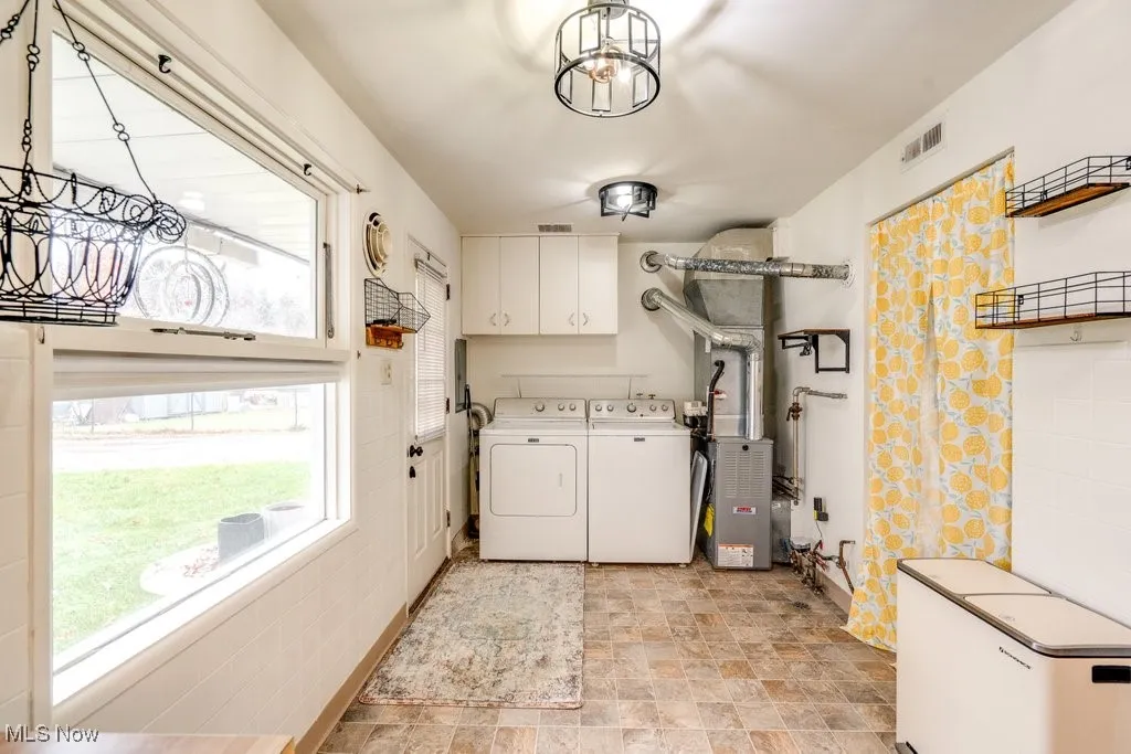 Laundry room featuring cabinet space, washing machine and clothes dryer, stone finish flooring, a chandelier, and heating unit