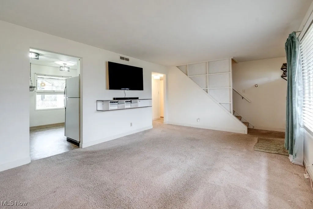 Unfurnished living room with light colored carpet and stairway