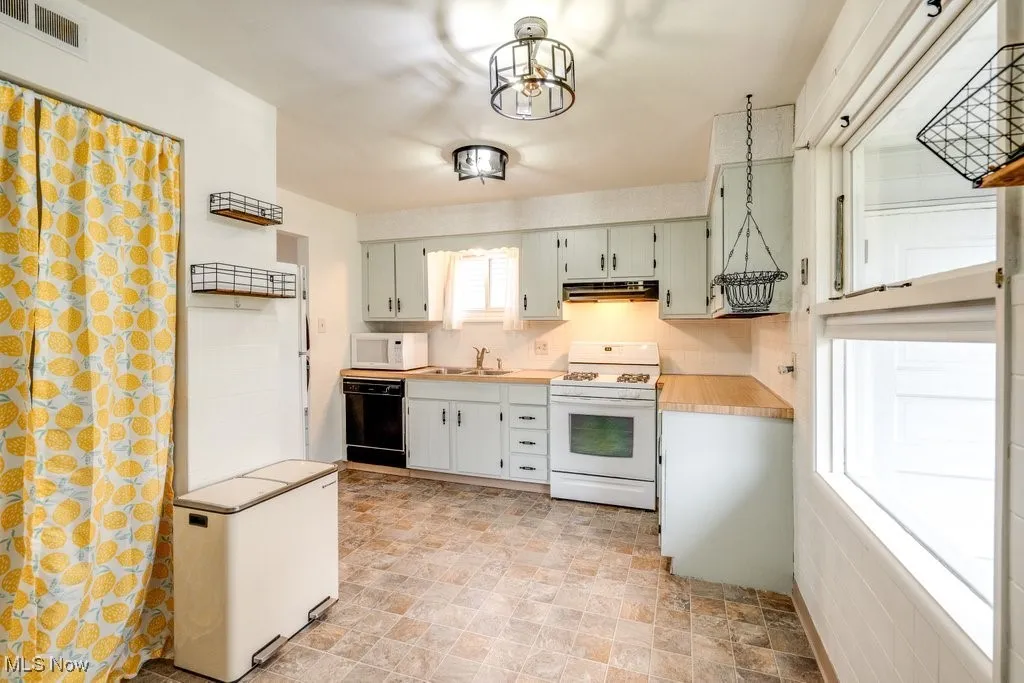 Kitchen featuring white appliances, light countertops, stone finish floors, under cabinet range hood, and green cabinetry