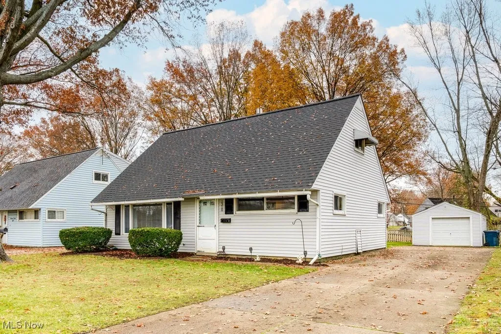 Cape cod house featuring an outbuilding, a shingled roof, concrete driveway, and a front yard