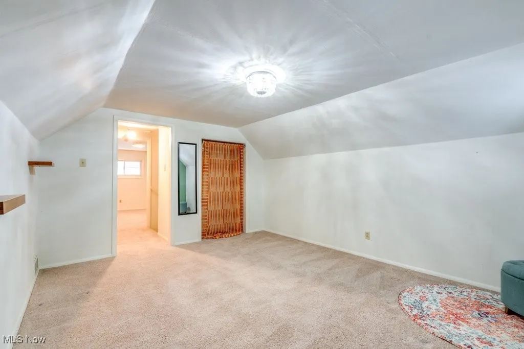 Additional living space with lofted ceiling and light carpet