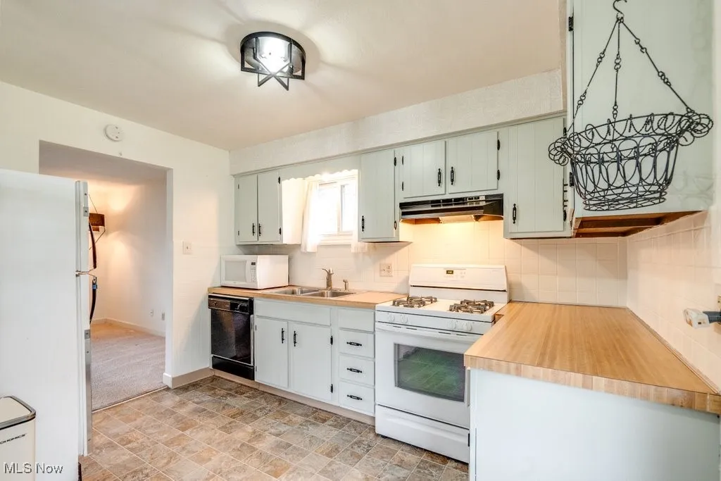 Kitchen featuring white appliances, decorative backsplash, light countertops, and under cabinet range hood