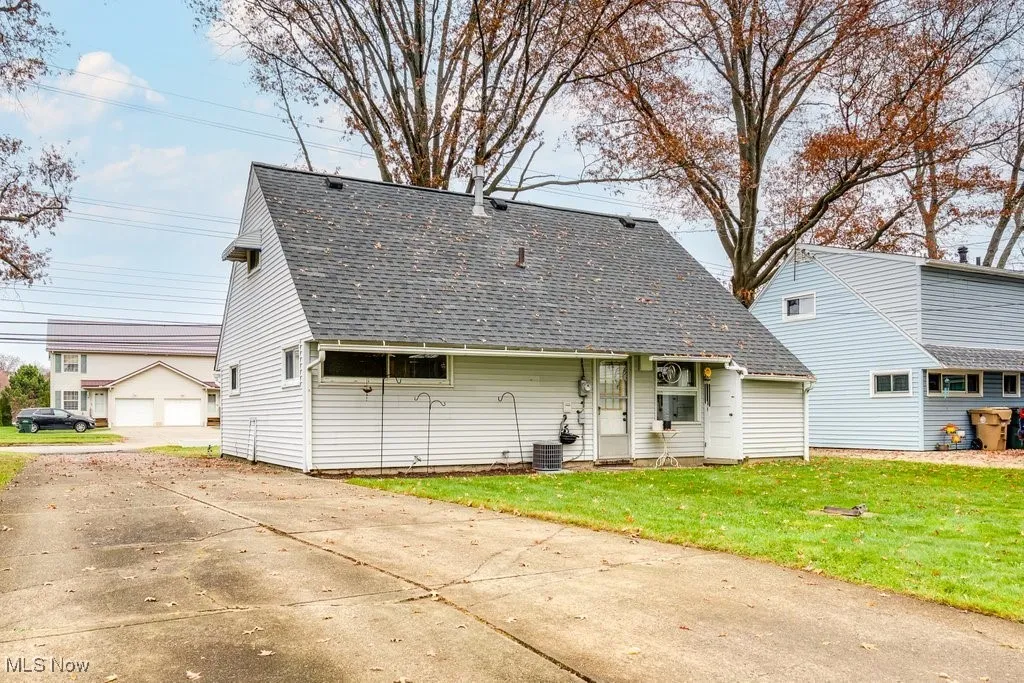 Rear view of house featuring a shingled roof, a yard, and a detached garage