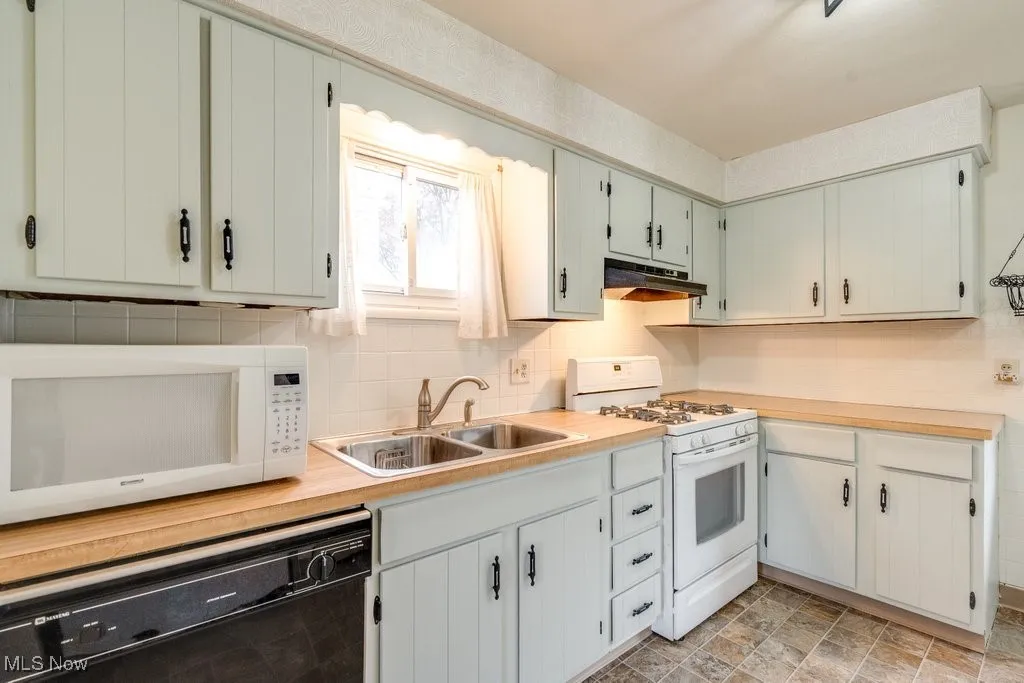 Kitchen with white appliances, light countertops, tasteful backsplash, under cabinet range hood, and stone finish flooring