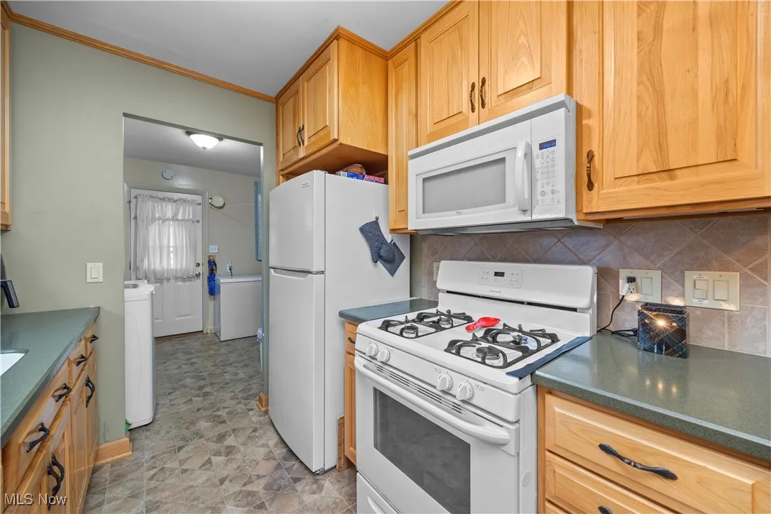 Kitchen featuring white appliances, tasteful backsplash, crown molding, and washer / dryer