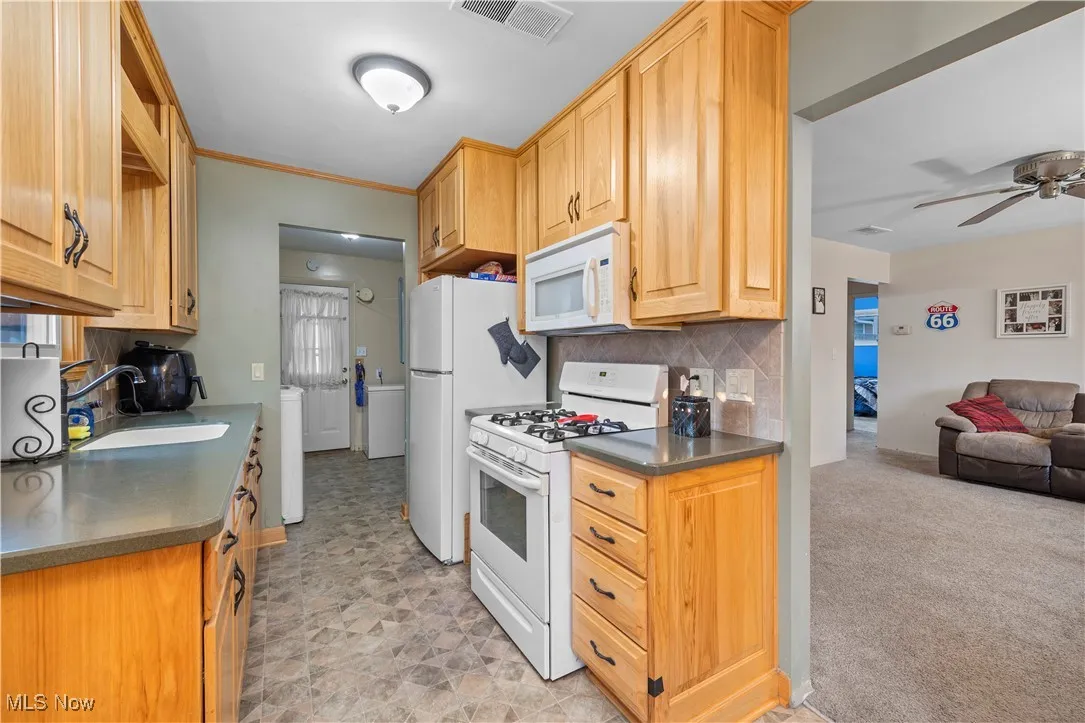 Kitchen with white appliances, tasteful backsplash, a ceiling fan, light brown cabinets, and open floor plan
