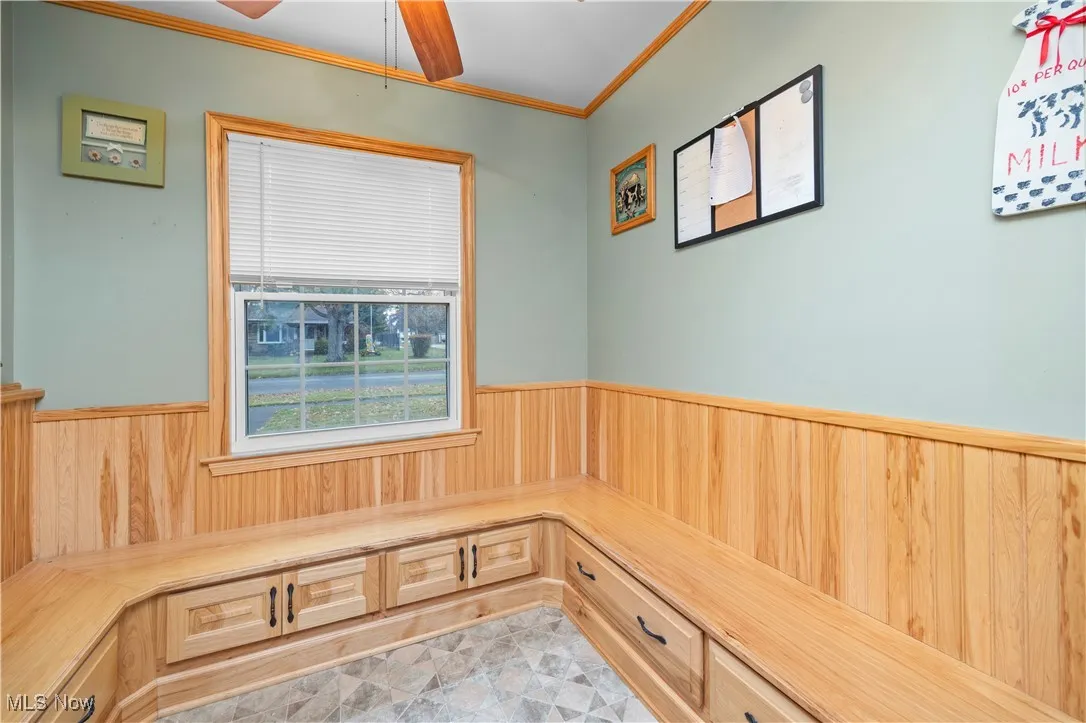 Breakfast / Dining area built in seating wainscoting, crown molding, wood walls, and a ceiling fan