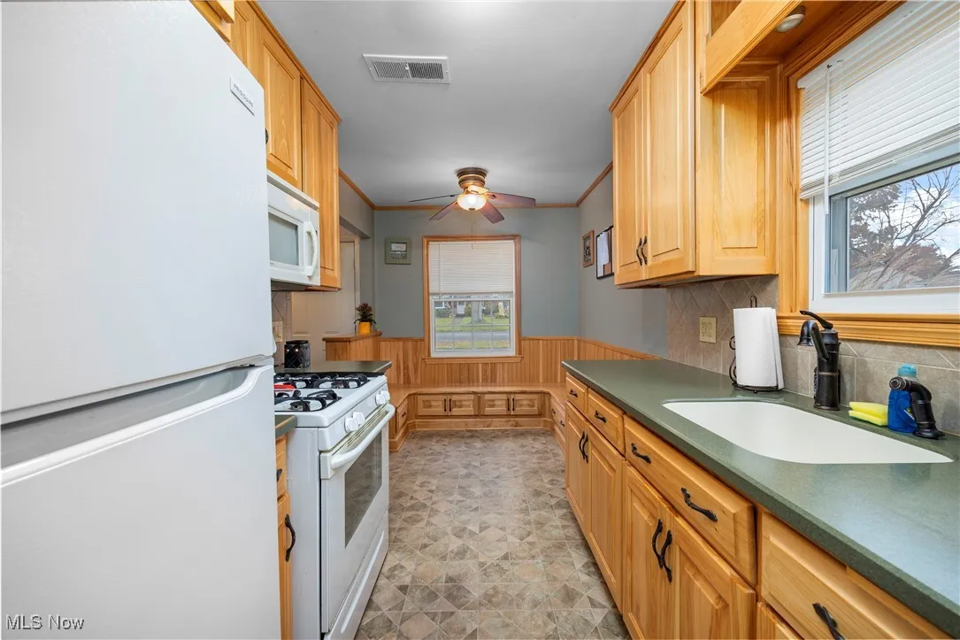 Kitchen with dark countertops, white appliances, a wainscoted wall, ornamental molding, and wood walls