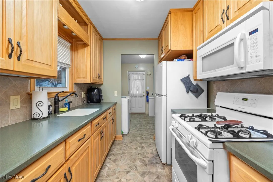 Kitchen with white appliances, decorative backsplash, dark countertops, ornamental molding, and stone finish floors