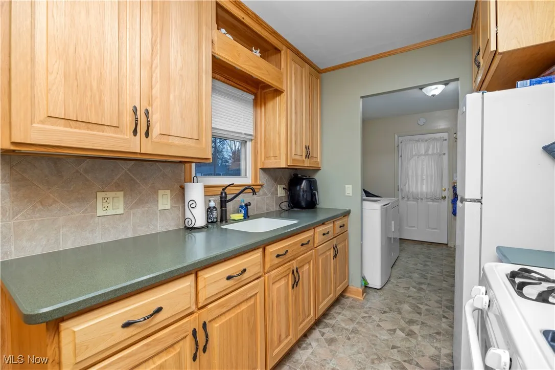 Kitchen featuring tasteful backsplash, dark countertops, ornamental molding, white range with gas stovetop, and washer and clothes dryer
