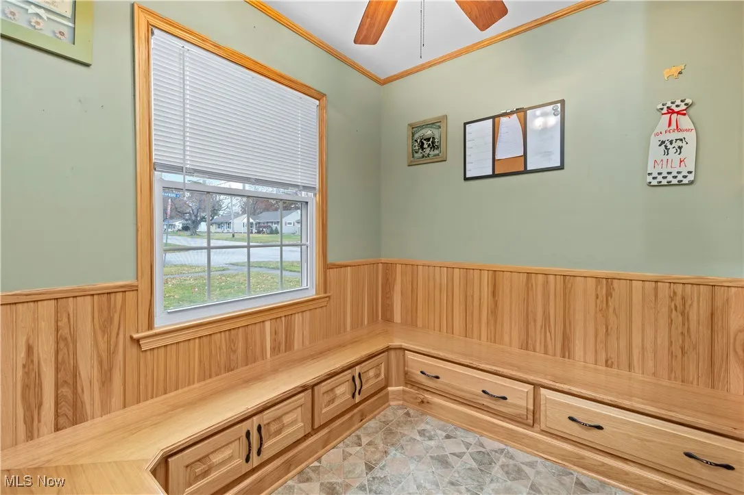 Breakfast / Dining area built in seating wainscoting, crown molding, wood walls, and a ceiling fan