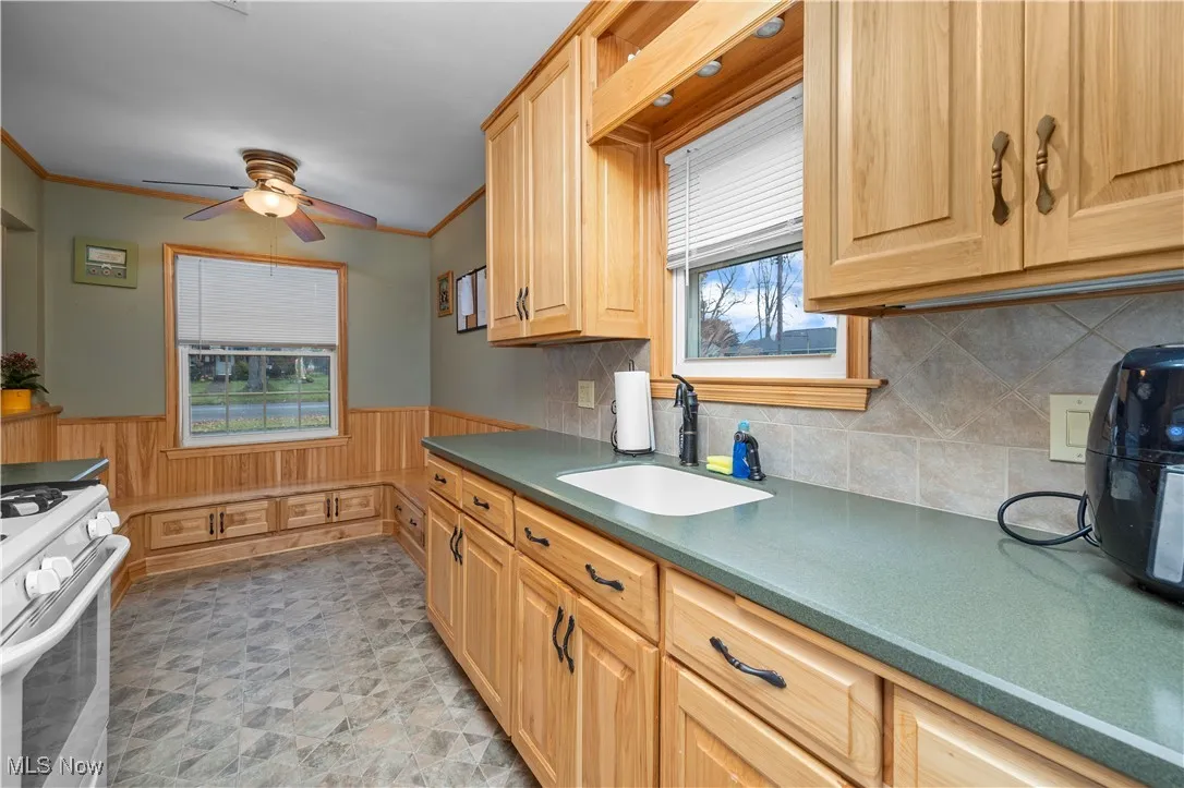 Kitchen with wainscoting, gas range gas stove, healthy amount of natural light, dark countertops, and ornamental molding