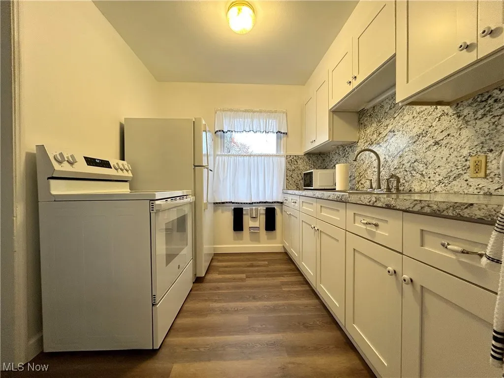 Kitchen with white appliances, tasteful backsplash, white cabinetry, and dark wood-style flooring
