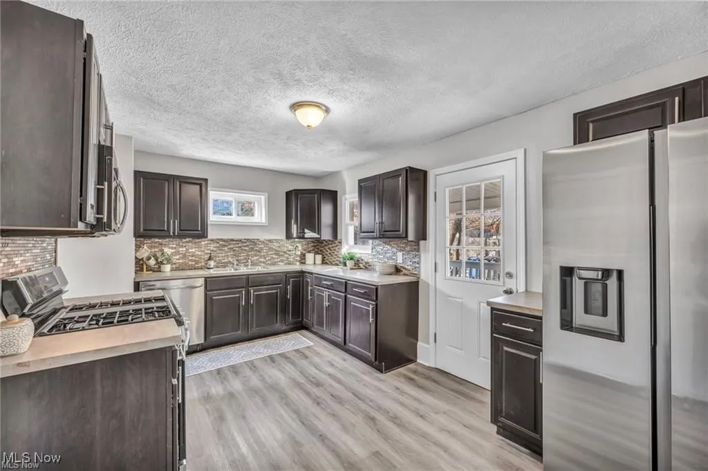 Kitchen with appliances with stainless steel finishes, dark brown cabinetry, light countertops, and a textured ceiling
