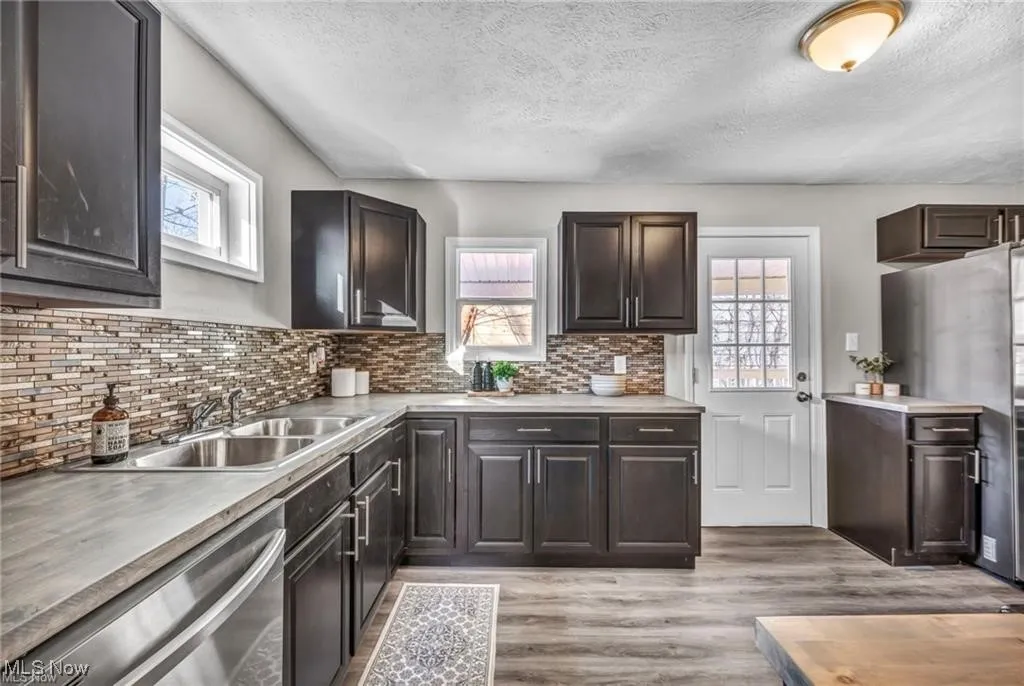 Kitchen with stainless steel appliances, healthy amount of natural light, a textured ceiling, light wood-style floors, and light countertops
